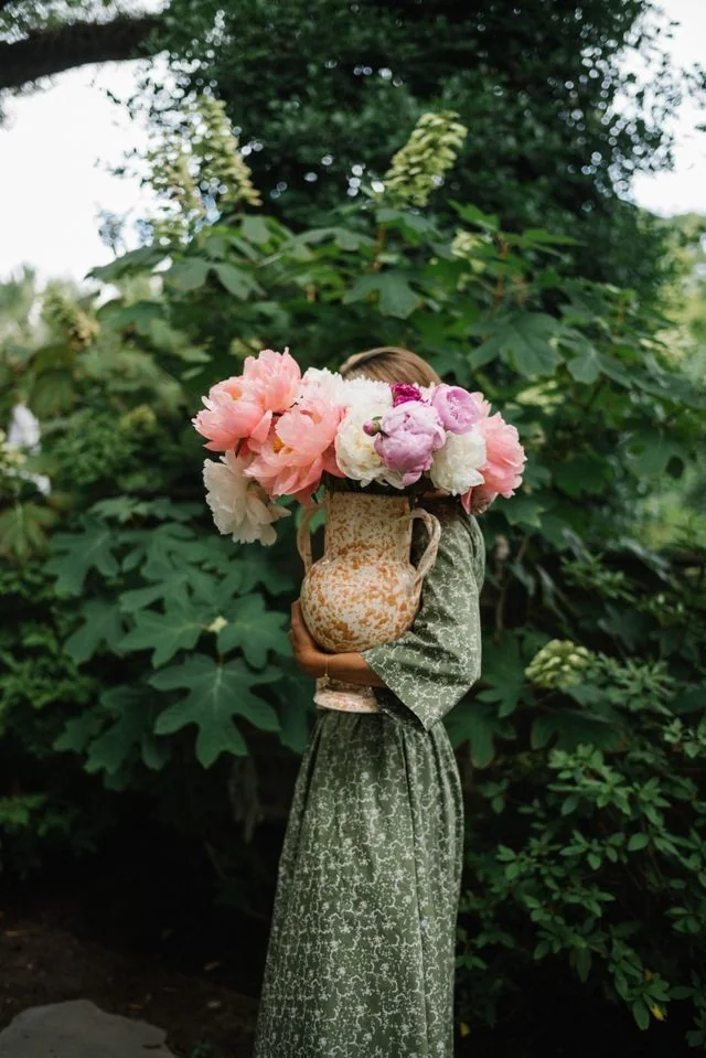 A wicker basket holding blush and white garden flowers against deep green foliage.