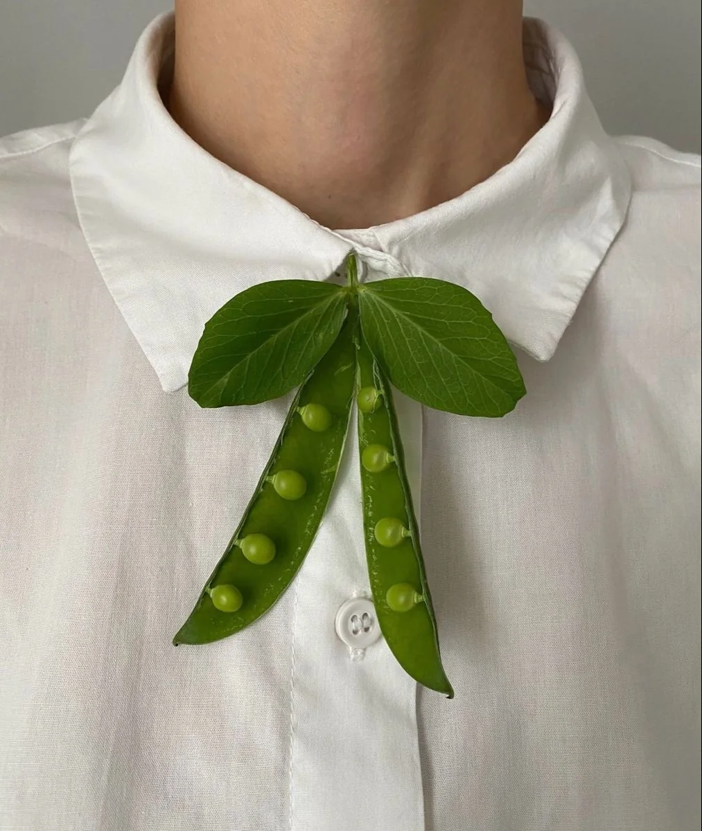 A bow-like botanical detail made from broad green leaves on a white shirt.