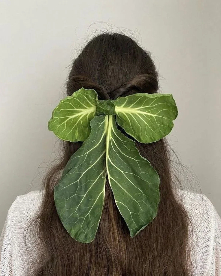 Large green leaves arranged as a bow over dark hair seen from behind.