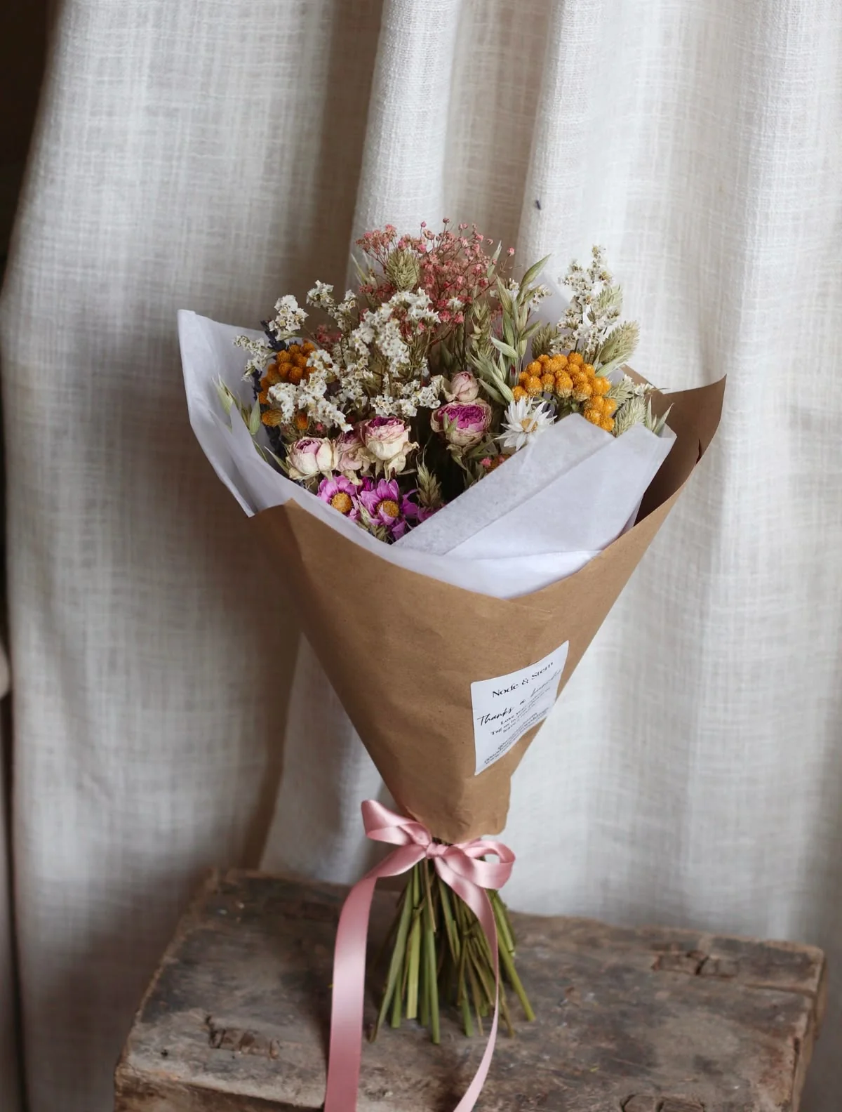 A ribbon-tied bouquet of mixed botanicals beside a softly lit window.