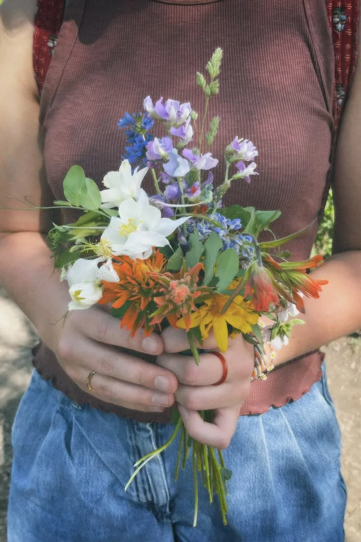 A loose hand-held posy of blue, white and yellow seasonal flowers.